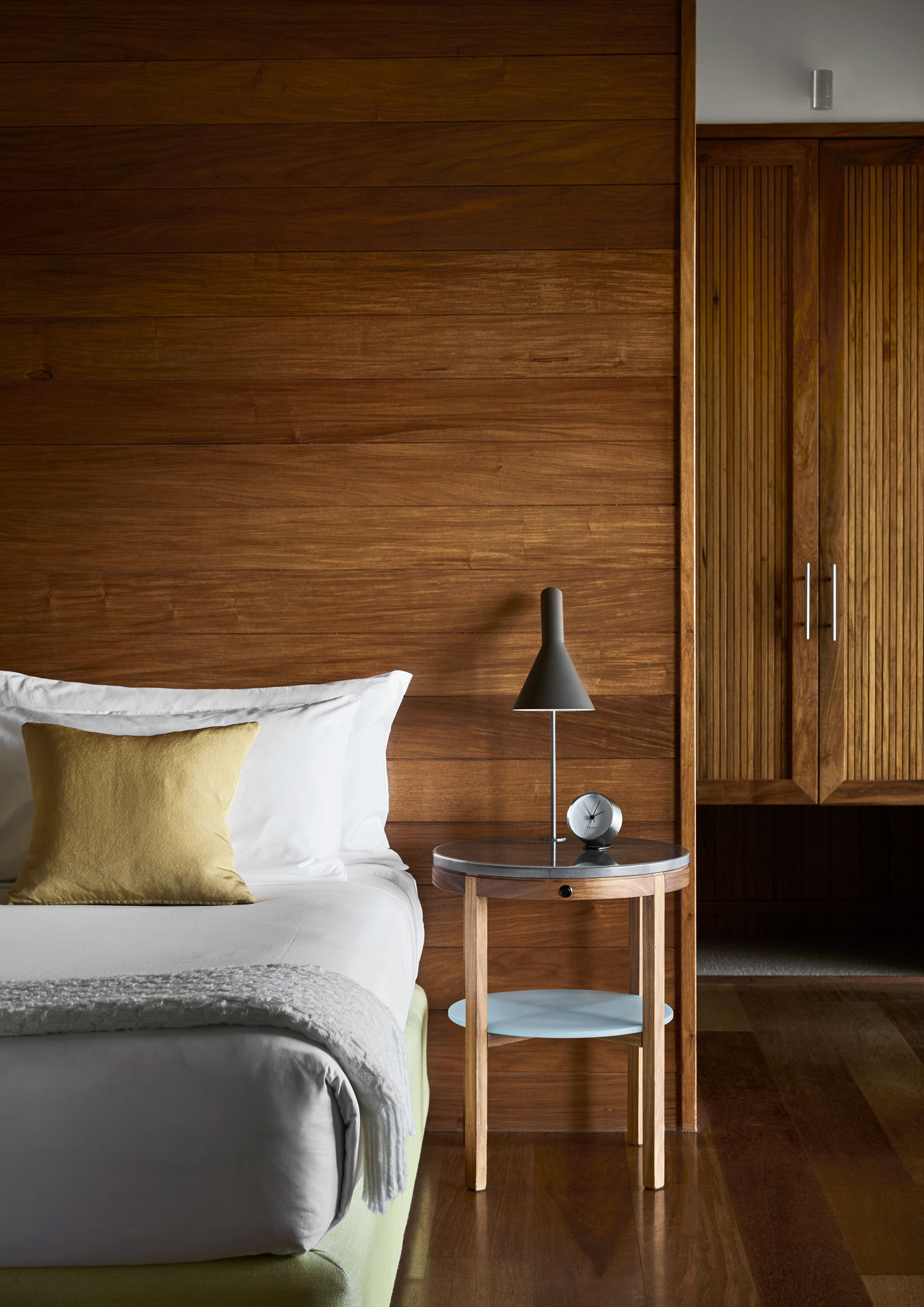 Bed with lamp and alarm clock on side table and wooden wall panelling in qualia resort Leeward Pavilion bedroom